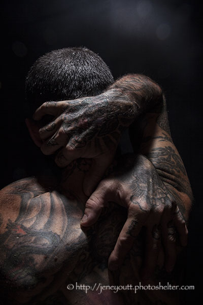 Tattooed male grasping his head and shoulders.
